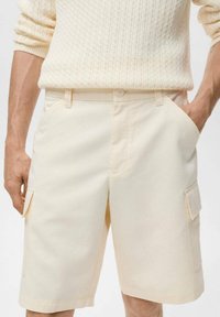 Shorts cargo beiges avec deux poches latérales et deux poches à rabat, fabriqués en coton, dotés d'une fermeture à bouton et d'une coupe décontractée.