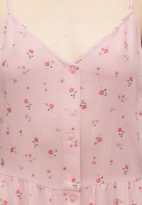 Ροζ αμάνικο φόρεμα με λεπτές τιράντες, κουμπωτό μπροστινό μέρος και μικρό διάσπαρτο ροζ λουλουδένιο μοτίβο σε ελαφρύ ύφασμα.