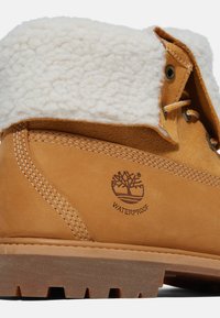 Botte imperméable beige avec un col en fausse fourrure blanche, des coutures renforcées et une semelle en caoutchouc texturé avec un logo d'arbre embossé.