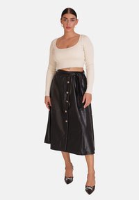 Schwarzer Rock aus Kunstleder mit hoher Taille, vorderen Knöpfen und seitlichen Bindebändern, kombiniert mit einem hellen, gerippten, kurz geschnittenen Langarmshirt.