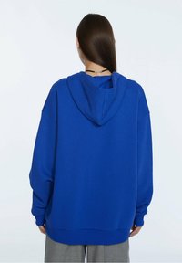 Felpa oversized blu con cappuccio regolabile, polsini e fondo a costine, realizzata in tessuto morbido, con una texture liscia e una vestibilità comoda.