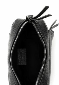 Borsetta nera in pelle con superficie testurizzata, chiusura superiore con cerniera e due brevi cinturini in pelle. Etichetta interna minimalista visibile all'interno.