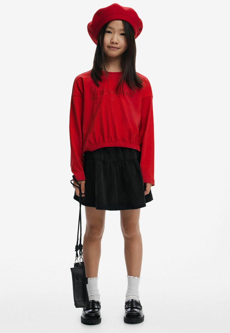 Roter, kurzer Sweatshirt mit dekorativem Text, schwarzer Denim-Rock, weiße Knöchelsocken und schwarze Plattformslipper. Rote Beret und kleine schwarze Tasche.