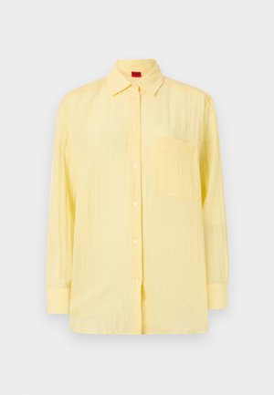 Yellow long-sleeve shirt with a button-down collar, single chest pocket, and a textured fabric. Features white buttons and a relaxed fit.