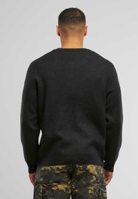 Schwarzer Strickpullover mit Rundhalsausschnitt, gerippten Bündchen und Saum; kombiniert mit mehrfarbigen Cargo-Hosen. Der Stoff hat eine glatte Textur.