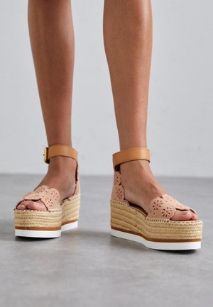 Sandalias de plataforma de esparto en color durazno con recortes florales, correa para el tobillo en tono claro y media suela de yute trenzado, que presenta una suela de goma blanca.