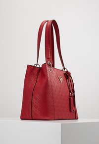 Rode synthetische totebag met reliëfpatroon, twee schouderbanden en gouden accenten. Beschikt over een afneembare label en een gestructureerde vorm.