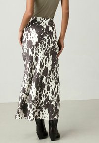 Jupe tachetée marron et blanche au design fluide, faite en tissu lisse, avec une taille haute et un léger évasement au bas.