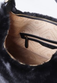 Zwarte nepbont handtas interieur met een beige voering die een herhaald logo-patroon bevat, een ritssluiting vak en gouden hardware.