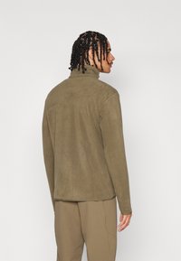 Men's olive green jacket made of smooth material, featuring a high collar and fitted sleeves. Simple, seamless design with no visible hardware.