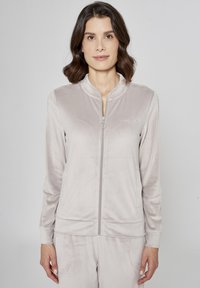 Jasnoszara kurtka zapinana na zamek z kołnierzem stójką i długimi rękawami, wykonana z miękkiego, gładkiego materiału; posiada haftowane logo i suwak z pierścieniem.