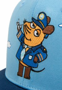 Blue cap featuring embroidered cartoon character dressed as a pilot, with brown details, in a blue uniform against a sky background.