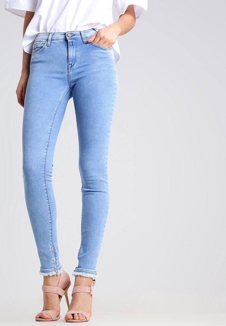 Jeans skinny azzurri chiari in denim, con vita alta, orlo sfilacciato e dettaglio con zip alla caviglia. Indossati con una camicia bianca e tacchi.