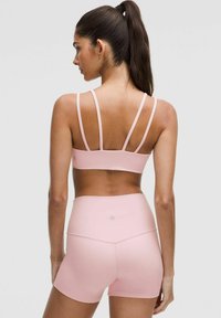 Light pink sports bra with multiple thin straps, paired with matching high-waisted shorts. Smooth, stretchy material with a fitted design.