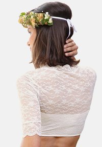 Lace crop top in ivory with floral pattern and short sleeves. Features scalloped edges and a high neckline. Flower crown accent.