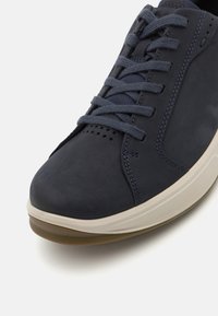Navy blue leather sneaker with a smooth texture, round toe, contrasting light sole, and grey laces. Features ventilation holes and stitching details.