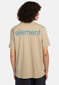 Beige bomulds t-shirt med korte ærmer og rund hals. Har et blåt grafisk logo på ryggen med teksten "element" og "SKATEBOARD CO. WORLDWIDE."