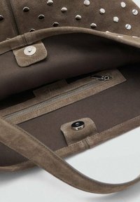 Intérieur d'un sac à main en suède marron avec des clous en argent, une poche zippée et un fermoir à pression. Présente une texture douce et une doublure en tissu contrasté.