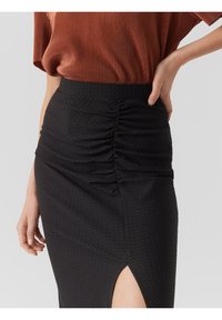 Jupe noire texturée avec un détail froncé sur le côté et une fente haute sur la cuisse. Associée à un haut marron côtelé.