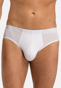 Männlicher Oberkörper und Oberschenkel, die schlichte weiße Slips mit einem passgenauen, nahtlosen Design und flach genähtem Bund tragen.