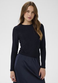 Námornícky dlhý rukáv s textúrovanou, lesklou látkou, s okrúhlym výstrihom a priliehavým strihom, spárovaný s hladkou tmavou sukňou.