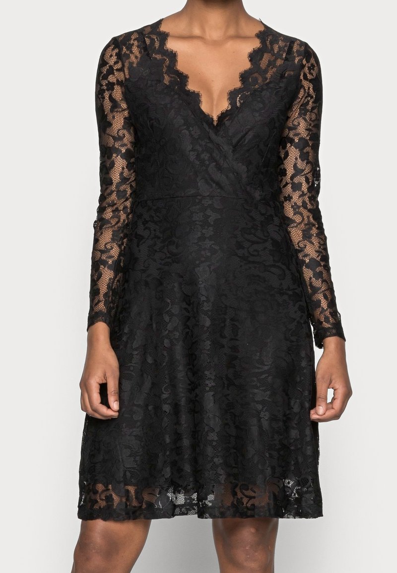 Czarna koronkowa sukienka z długim rękawem, z kwiatowymi wzorami, dekoltem w kształcie litery V, dopasowaną talią i spódnicą o kroju A długości do kolan na osobie.