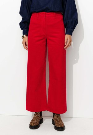 Un pantalon large en velours côtelé rouge avec une surface texturée. Associé à des bottines chelsea à imprimé léopard noir. Le modèle porte un haut en denim bleu.