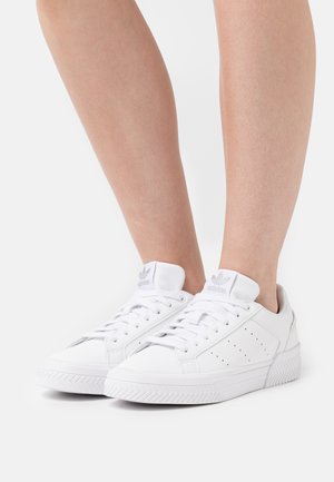 Zapatillas blancas con un acabado de cuero suave, puntas redondeadas, cordones planos y una suela de goma texturizada; cuenta con acentos perforados y detalle de logo.