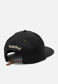 Cappello nero con visiera curva, realizzato in tessuto, con fori in ottone. "Timberland" ricamato in crema sul retro con cinturino regolabile.