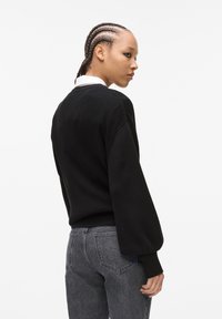 Mustmustest mustriibuline kootud sviiter, millel on lõdvestunud istuvus, pikkade varrukatega ja ümar kaelus, koos hallide kõrge vöökohaga teksadega.