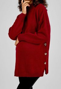 Suéter rojo de punto con cuello alto, con puños acanalados y detalles de botones laterales para un toque adicional. Material texturizado y ajuste relajado.