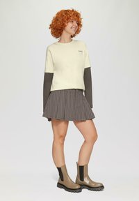Jasny, skrócony sweatshirt z ciemnymi rękawami, w połączeniu z plisowaną spódnicą w paski. Brązowe botki za kostkę z elastycznymi bokami.