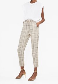 Pantalons à carreaux beiges avec une coupe fuselée, taille élastique et poches latérales, associés à un haut à manches courtes blanc et des talons dorés à lanières.