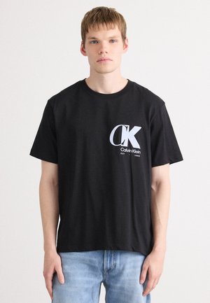 Zwarte katoenen t-shirt met een groot wit Calvin Klein-logo op de linkerborst, korte mouwen en een relaxte pasvorm.