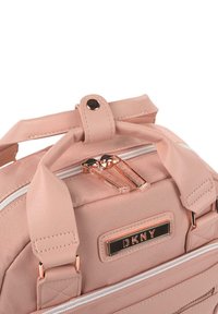 Bolso de tela rosa claro con un acabado texturizado, que presenta un cierre con cremallera, asas dobles y una placa del logo de DKNY en dorado. Acabado con herrajes en oro rosa.