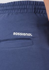 Granatowe dresy wykonane z miękkiego materiału, z elastycznym paskiem w talii, małą kieszonką i białym logo "ROSSIGNOL".