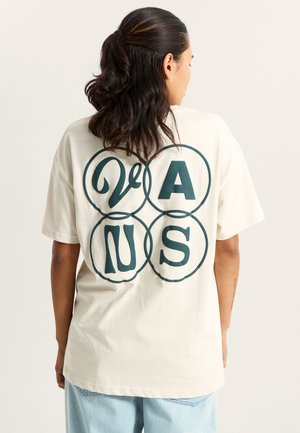 Cremefarbener Baumwoll-T-Shirt mit einem großen grünen Grafikdesign auf dem Rücken, das die Buchstaben "VAN" und "S" in einem kreisförmigen Muster zeigt. Kurze Ärmel.