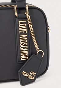 Black faux leather handbag with gold hardware, featuring a chain detail and two tags embossed with "LOVE MOSCHINO" in contrasting colors.