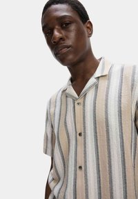 Korte mouwen shirt met verticale strepen in beige, wit en donkergrijs. Gemaakt van een gestructureerde stof met een notch-kraag en zwarte knopen.