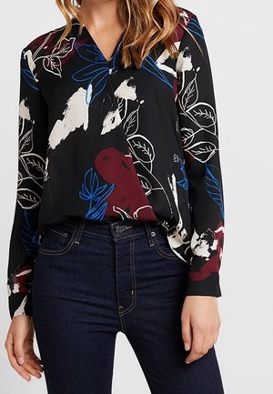 Zwarte blouse met kleurrijke bladeren en bloemmotieven in rood, wit en blauw; heeft een wikkelontwerp en lange mouwen, gecombineerd met donkere jeans.