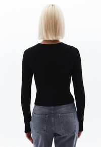 Maglietta nera a maniche lunghe a coste con design aderente, dotata di maniche raglan. Abbinata a jeans grigi in denim a vita alta con tasche posteriori.