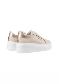 Sneaker in pelle beige con un accento metallico dorato sul tallone, suola piatta bianca e design classico con lacci.