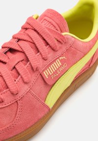 Baskets Puma Palermo en daim rose, avec des accents jaunes, des lacets plats et une semelle extérieure en caoutchouc gomme texturée. Logo affiché de manière bien visible sur le côté.