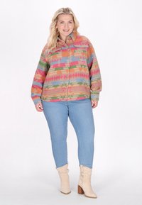 Färggad överstor skjorta med en geometrisk mönster i rosa, grön och blå. Bärs med ljusblå jeans och krämfärgade ankelskor.