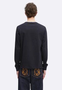 Zwarte longsleeve shirt met een ronde halslijn en een rechte zoom. Gecombineerd met donkerblauwe jeans, met astronautenafbeeldingen op de zakken.