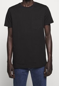 T-shirt nera in cotone con collo rotondo e maniche corte, dotata di una piccola tasca sul petto e dettagli di cucitura minimi.