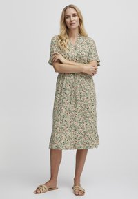Robe à imprimé floral avec décolleté en V, manches courtes et taille froncée, dans des teintes de vert, rose et noir. Associée à des sandales à glisser neutres.