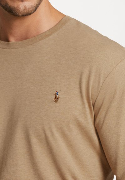 Μπεζ βαμβακερή μπλούζα t-shirt με στρογγυλή λαιμόκοψη. Διαθέτει ένα μικρό κεντητό λογότυπο ενός παίκτη polo στην αριστερή περιοχή του στήθους.