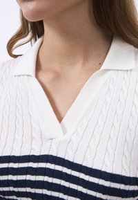 Polo à manches courtes en tricot blanc avec un motif rayé bleu marine. Doté d'un design en maille texturée et d'un col en V.
