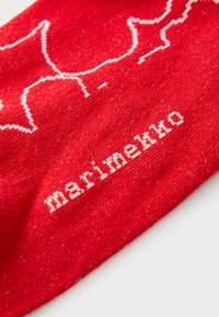 Tessuto rosso con un design mappale bianco lineare e la parola "marimekko" in bianco, che mostra un motivo a maglia testurizzata.